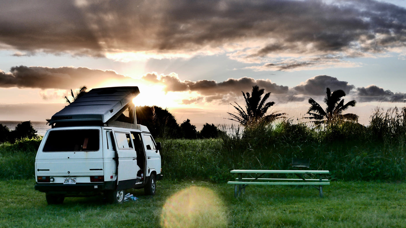 Relaxing sunset view with a white pop-top RV rental parked by the ocean and a picnic table. Perfect for camping!
