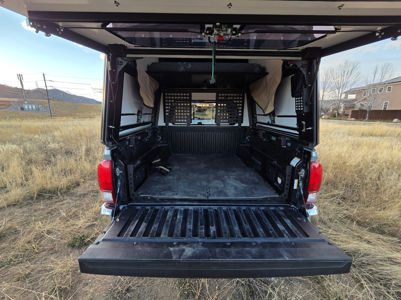 The open tailgate of an overland truck camper reveals a custom bed and storage for adventures. A unique RV rental option. — photo 8