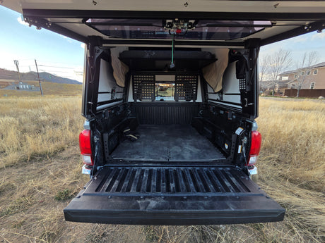 The open tailgate of an overland truck camper reveals a custom bed and storage for adventures. A unique RV rental option.