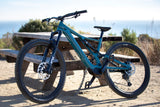 A teal Specialized e-mountain bike is parked by a picnic table, with an ocean view in the background. Perfect for RV rental adventures.