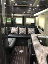 Inside a luxurious RV rental: rear black leather seating with patterned pillows, dark wood floors, and a sleek kitchenette.