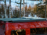 This red RV rental features rooftop solar panels and a mesh cargo rack, set against a snowy forest, equipped for off-grid travel.
