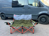 A Kelty two-person camping chair sits ready for relaxation beside a grey rv rental camper van, perfect for outdoor trips.