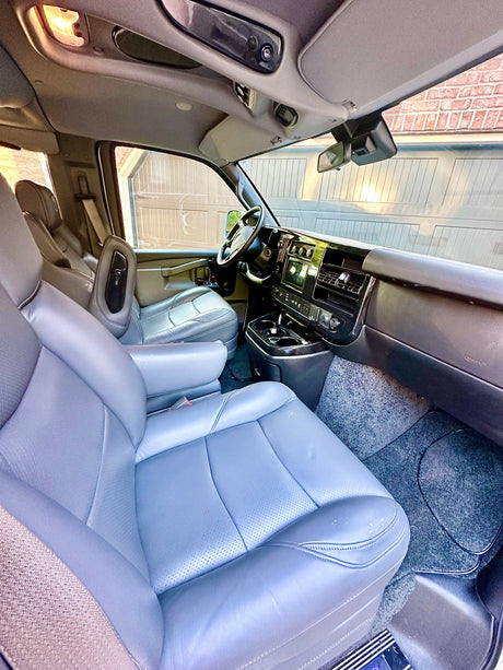 Experience comfort in this RV rental! Interior view of a spacious van, featuring plush gray leather seats, a modern dashboard, and bright cabin lighting.