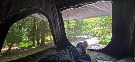 Relaxing in an RV rental, feet up, enjoying green trees & a road with cars & a cyclist. A great camp view.
