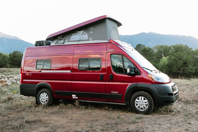 Red Winnebago Solis pop-top RV rental parked in a scenic mountain landscape, ready for adventure.