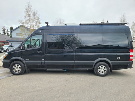 Black Mercedes-Benz Sprinter RV rental, marked 218, with solar panels, parked in a suburban setting.