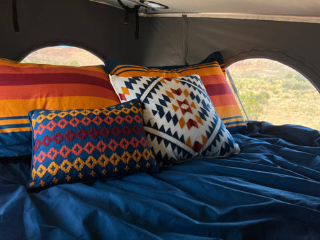 Cozy bed in an RV rental, featuring vibrant southwestern pillows, blue sheets, and a serene desert view.