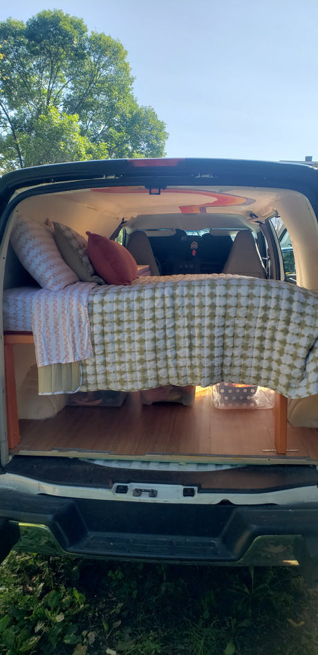 Cozy camper van interior, perfect for an RV rental or van life adventure. Bed with storage & wood floor.