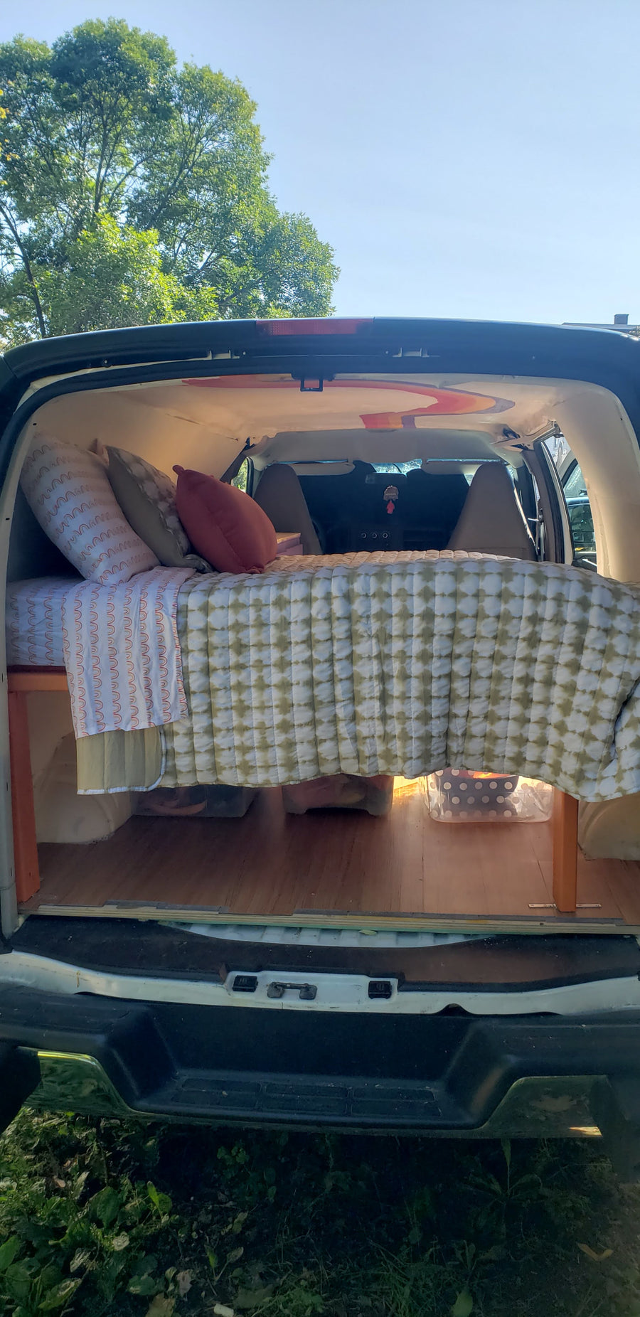Cozy camper van interior, perfect for an RV rental or van life adventure. Bed with storage & wood floor.