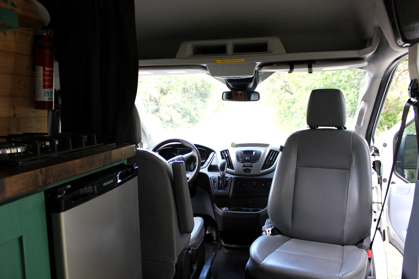 RV rental van interior: a kitchen area with stove, Frigidaire fridge, fire extinguisher, and the driver's cabin.