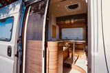Explore a modern RV rental's inviting, wood-finished interior. Features include a dining area, storage, and a pleated screen door.