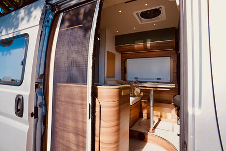 Explore a modern RV rental's inviting, wood-finished interior. Features include a dining area, storage, and a pleated screen door.