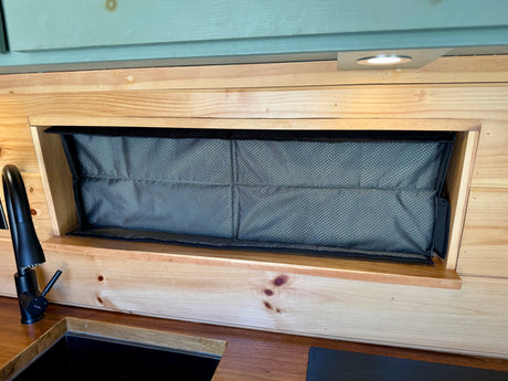 Modern RV rental kitchen features wooden paneling, black faucet, sink, and a practical mesh fabric storage compartment.