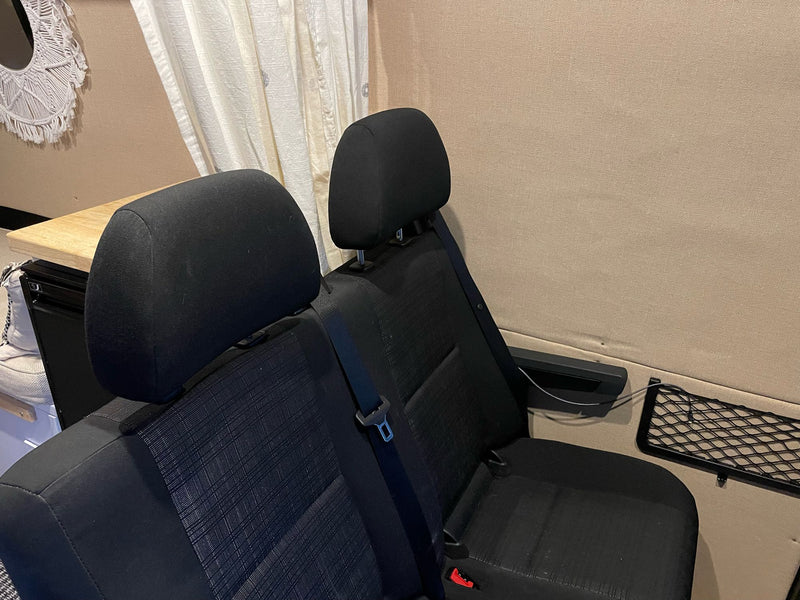 RV rental interior featuring two black passenger seats, a wooden table, and beige wall paneling. — photo 19
