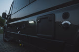 Evening view of an RV rental side, highlighting illuminated light, water inlet ("CITY FILL"), and other utility access points.