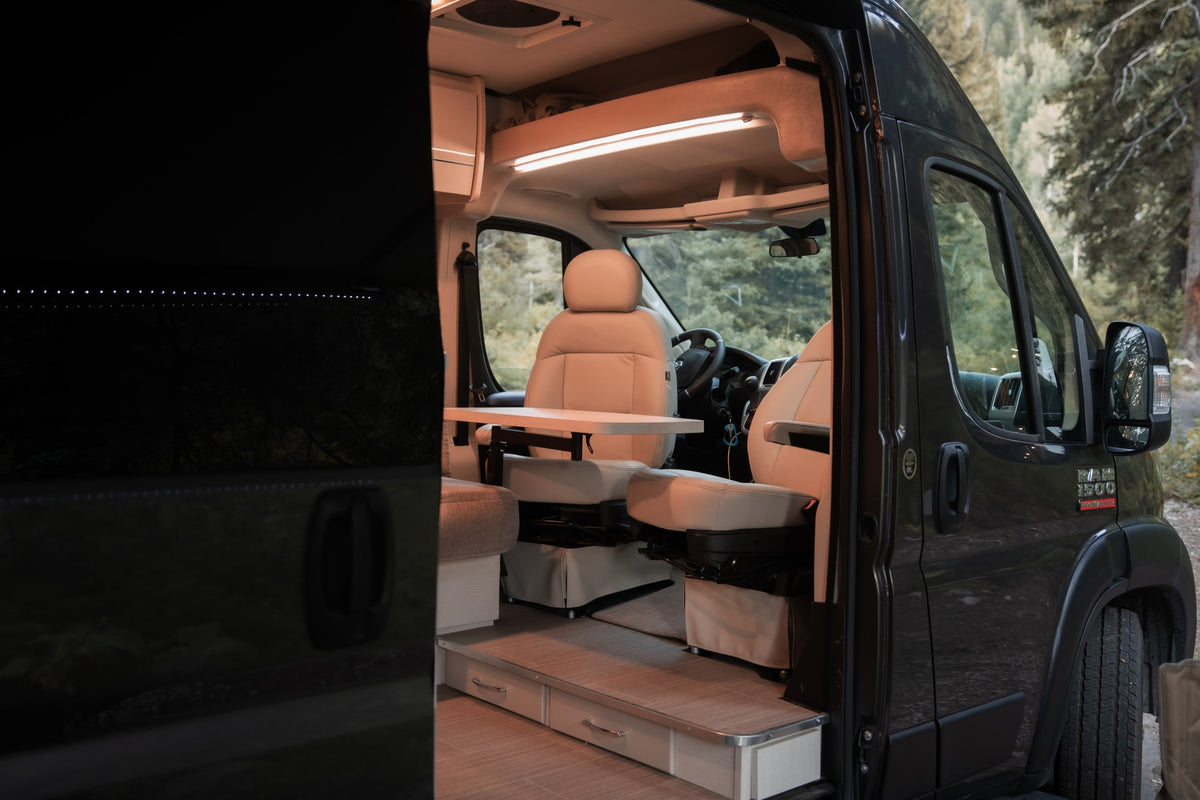 Inside a modern rv rental camper van: swiveling light-colored seats, a movable dining table, and LED strip lighting. — photo 7