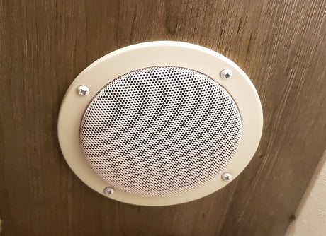 Circular beige speaker or vent with a perforated grille, mounted on wood paneling inside an RV rental.