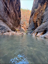 Wading through Zion Narrows river, person in waders surrounded by towering canyon walls. Perfect RV rental trip.