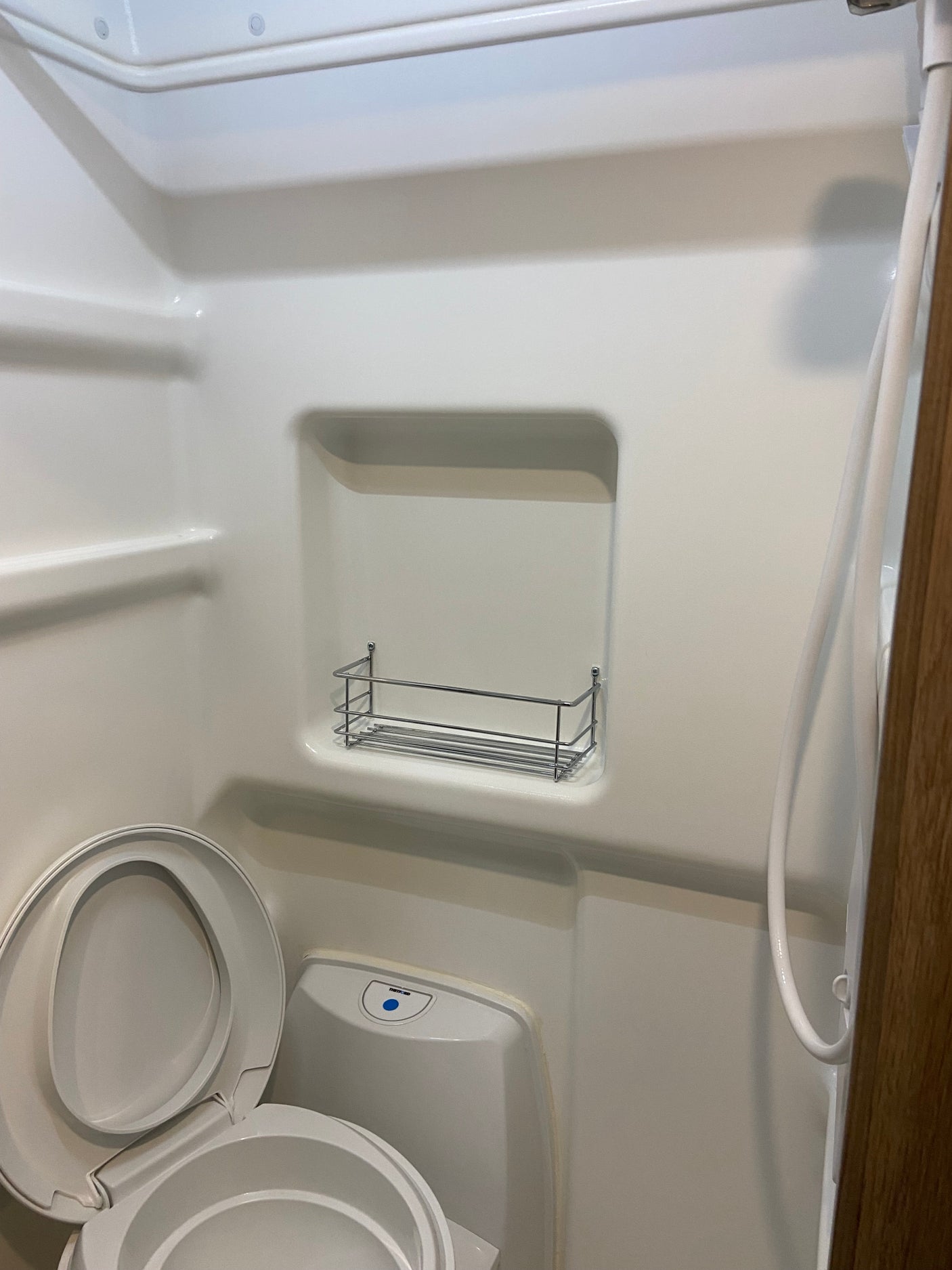 RV rental wet bath with white toilet, open lid, shower hose, and integrated storage.