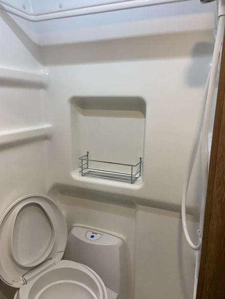 RV rental wet bath with white toilet, open lid, shower hose, and integrated storage.