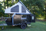 RV rental: A gray and black off-road adventure trailer with an open pop-up tent and storage, ready for camping.