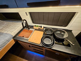 Compact RV rental kitchen and bedroom area featuring a sink, cooktop, bed, and stylish lighting for comfortable travel.