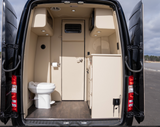 Inside a luxurious RV rental, showing the compact bathroom with a toilet and a small kitchen area with a microwave.