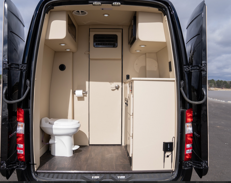 Inside a luxurious RV rental, showing the compact bathroom with a toilet and a small kitchen area with a microwave.