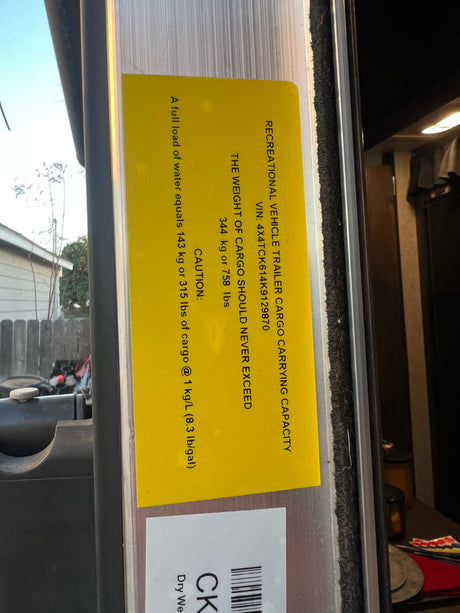 An RV rental's cargo capacity label, detailing max weight (344kg/758lbs) and water weight. Vital for safe loading.
