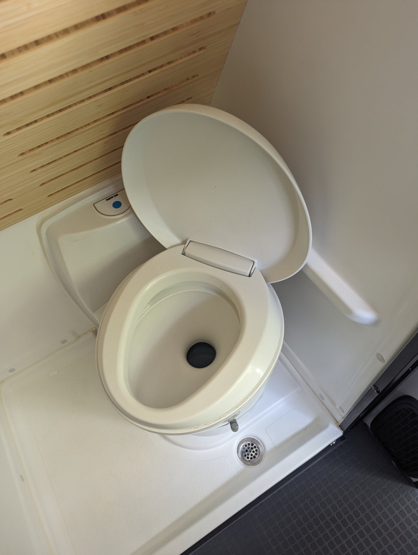RV rental compact wet bath: Thetford toilet with open lid, shower drain, and wooden slatted wall details.