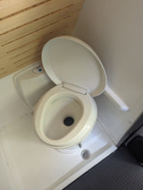 RV rental compact wet bath: Thetford toilet with open lid, shower drain, and wooden slatted wall details.