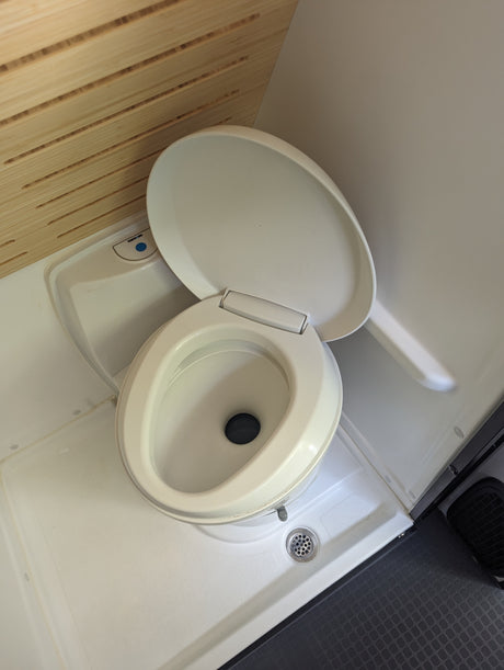 RV rental compact wet bath: Thetford toilet with open lid, shower drain, and wooden slatted wall details.