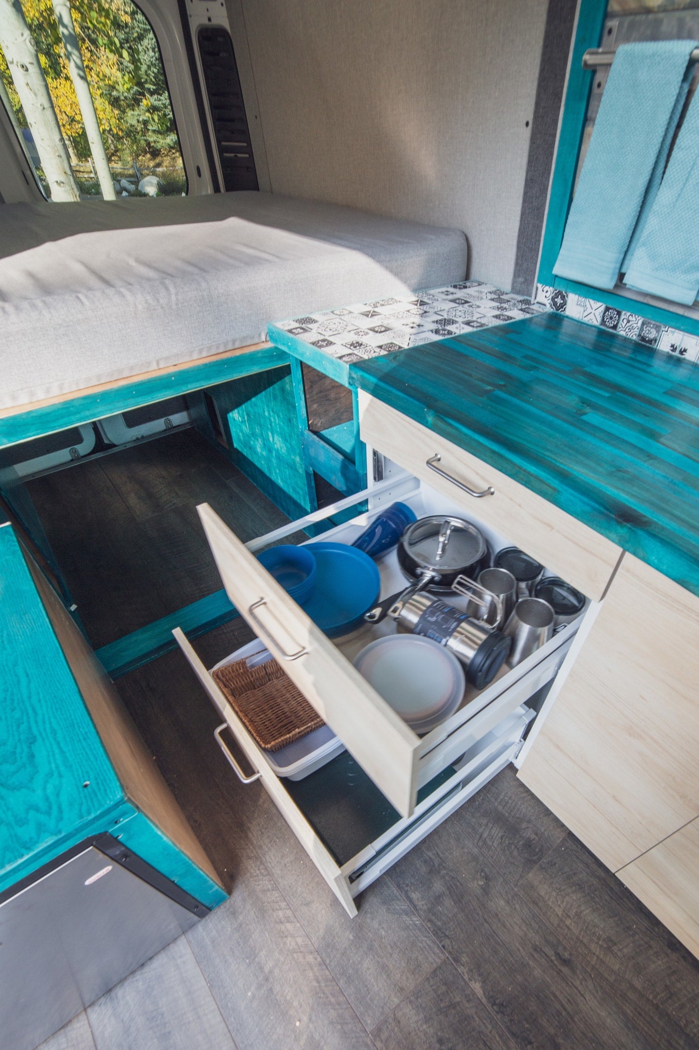 Explore this organized RV rental interior with a cozy bed and kitchen drawers packed with cooking essentials and dishes. — photo 5