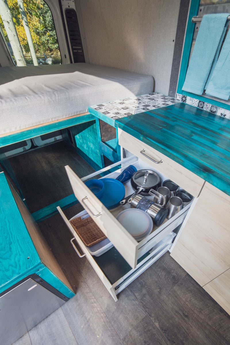 Explore this organized RV rental interior with a cozy bed and kitchen drawers packed with cooking essentials and dishes. — photo 5