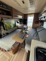 Cozy RV rental workspace with beds, a monitor, laptop, and scenic ocean views from the open rear.