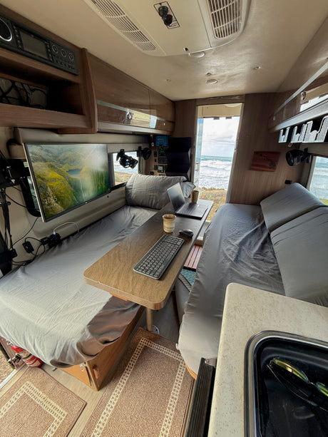 Cozy RV rental workspace with beds, a monitor, laptop, and scenic ocean views from the open rear.