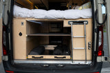 RV rental camper van's rear shows a raised bed, under-bed wooden storage with shelves, a pull-out drawer, and an access ladder.