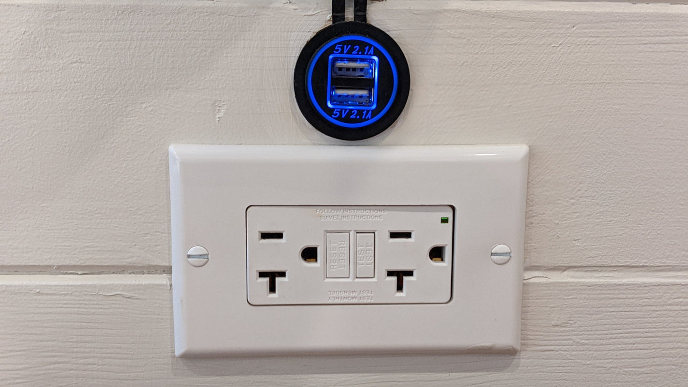 Dual USB charger (5V 2.1A) and GFCI electrical outlet on a textured wall in an RV rental.