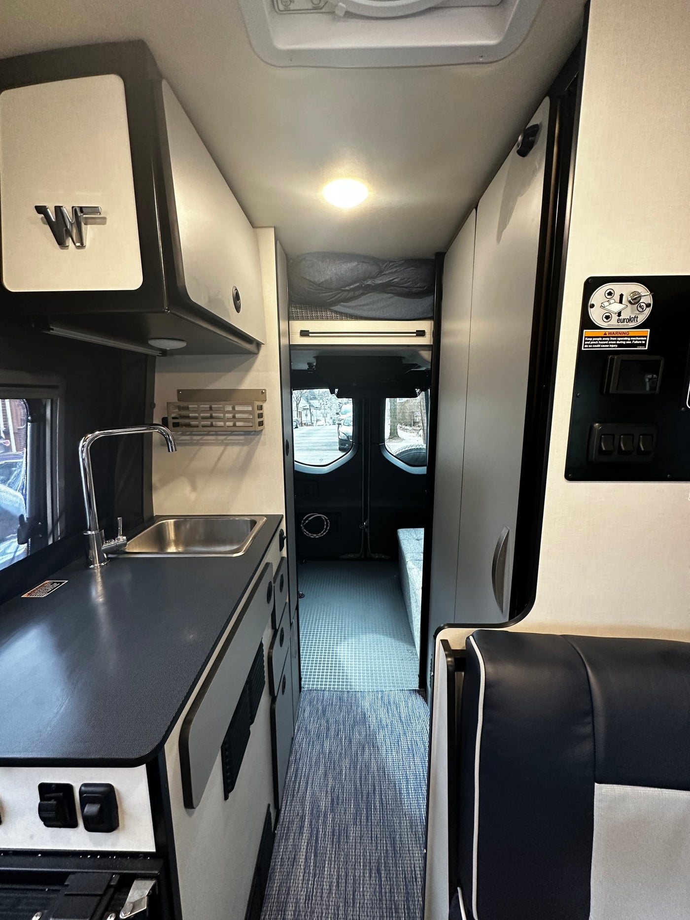 Inside an rv rental camper van, showing a compact kitchen, a rear sleeping area (Euroloft), and system controls. — photo 11