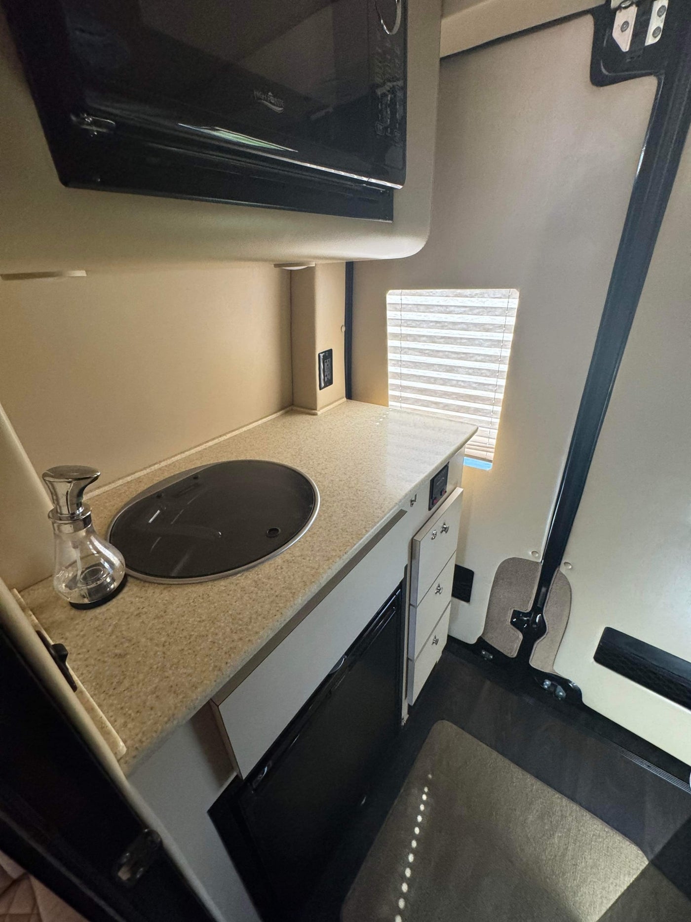 Step into this RV rental! Compact kitchen with microwave, cooktop, drawers, and window. — photo 16