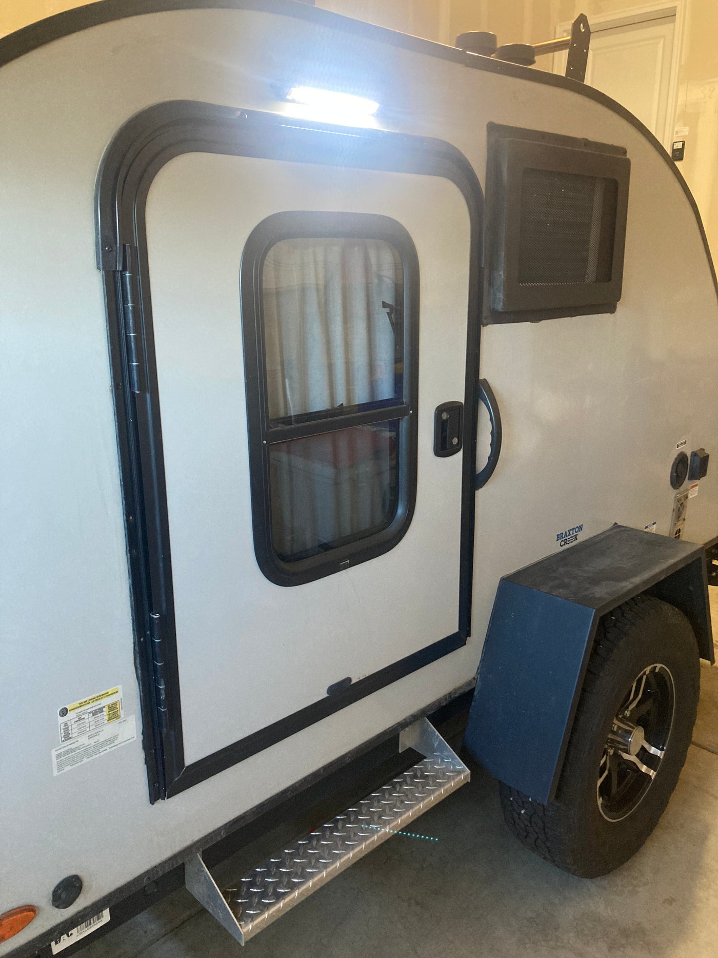 This RV rental, a Braxton Creek travel trailer, features a side door with window, bright exterior light, pull-out step, and wheel. — photo 14