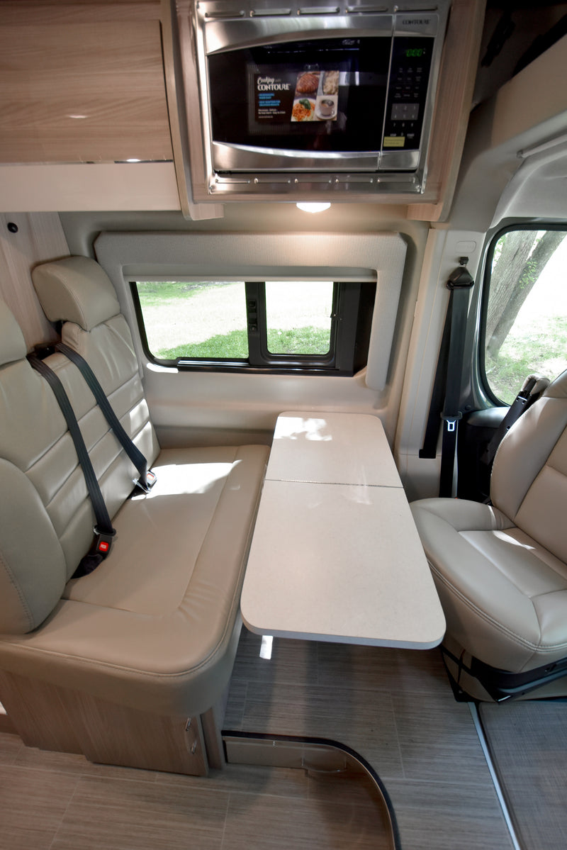 RV rental interior: Comfortable dining area with cream upholstered seats, a folding table, and a stainless steel microwave. — photo 3