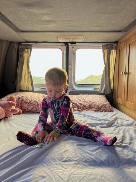 Cozy RV rental adventure: Toddler plays on the bed inside a camper van, sunlight streaming through windows.