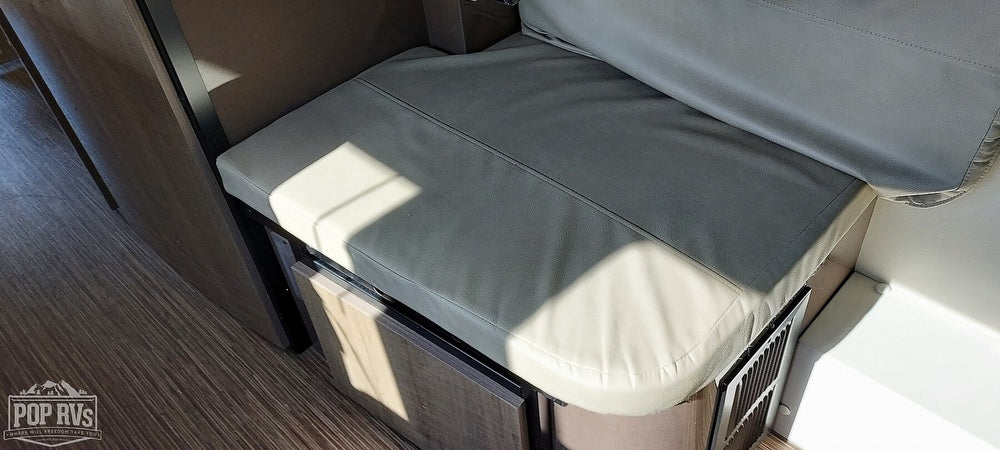 RV rental's cozy seating area with light gray cushions, wood cabinetry, and laminate flooring.