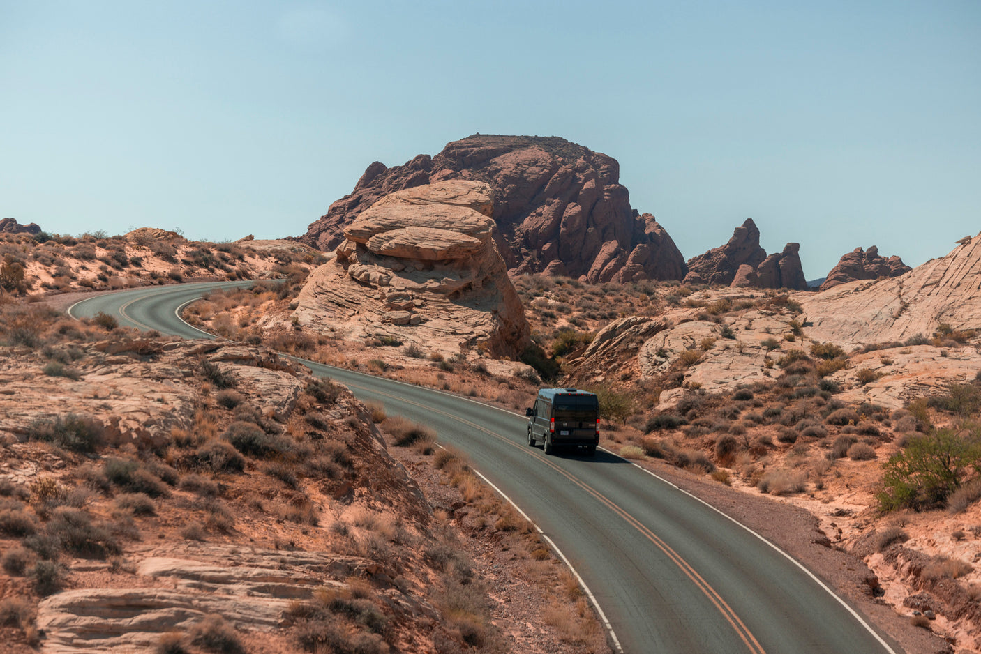 Black RV rental drives on a scenic desert road with red rock formations under a clear sky.