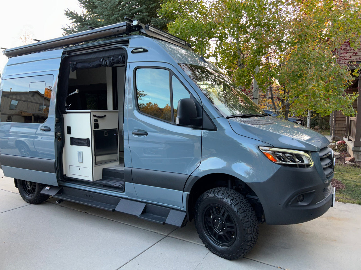 Sleek gray custom camper van, open side door reveals interior. Perfect for your next RV rental adventure on rugged terrains.