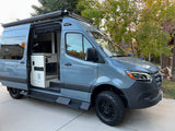 Sleek gray custom camper van, open side door reveals interior. Perfect for your next RV rental adventure on rugged terrains.