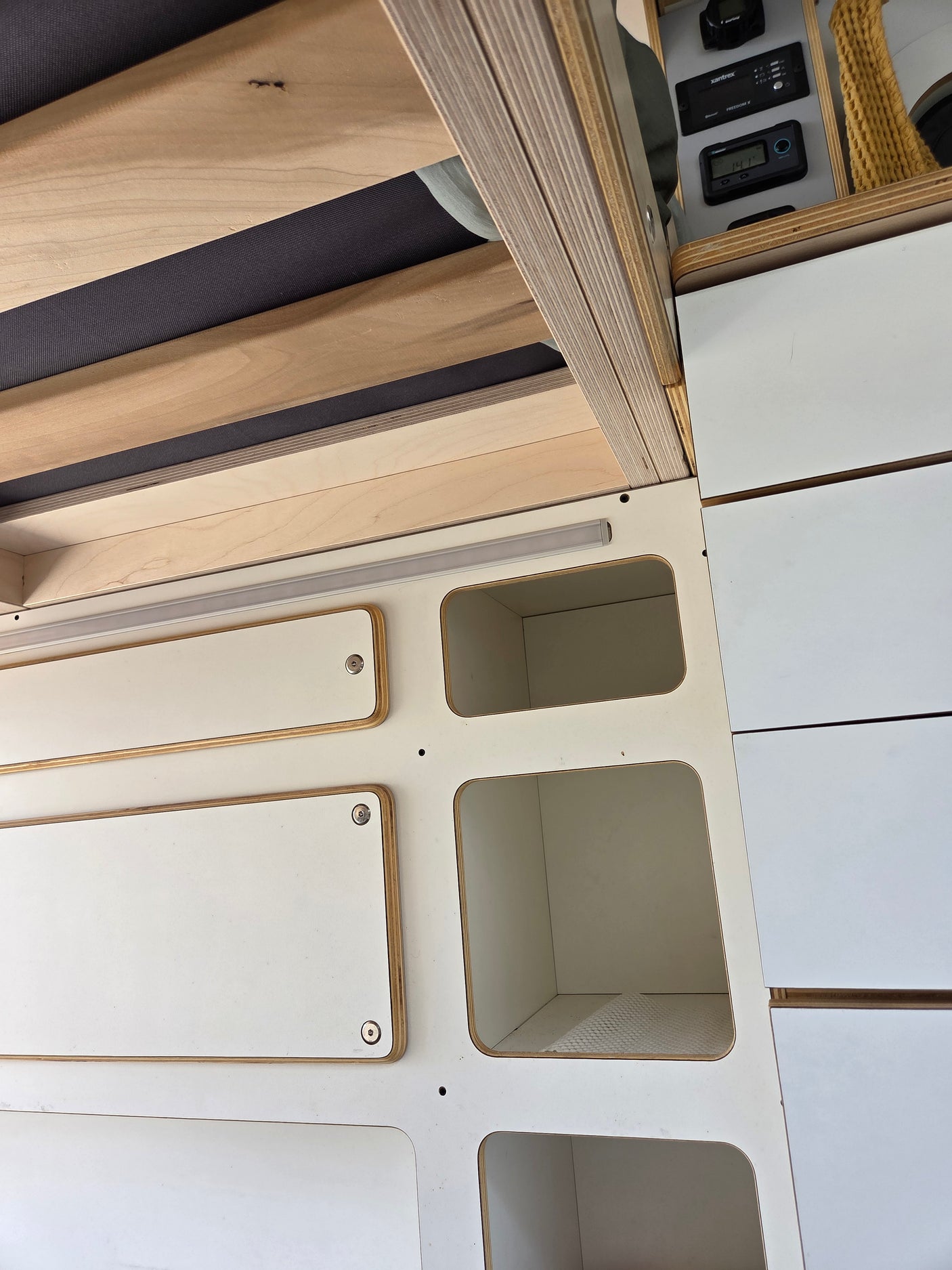 RV rental interior showcasing a wooden slatted bed, white modular storage, and an electrical control panel for a functional camper van.