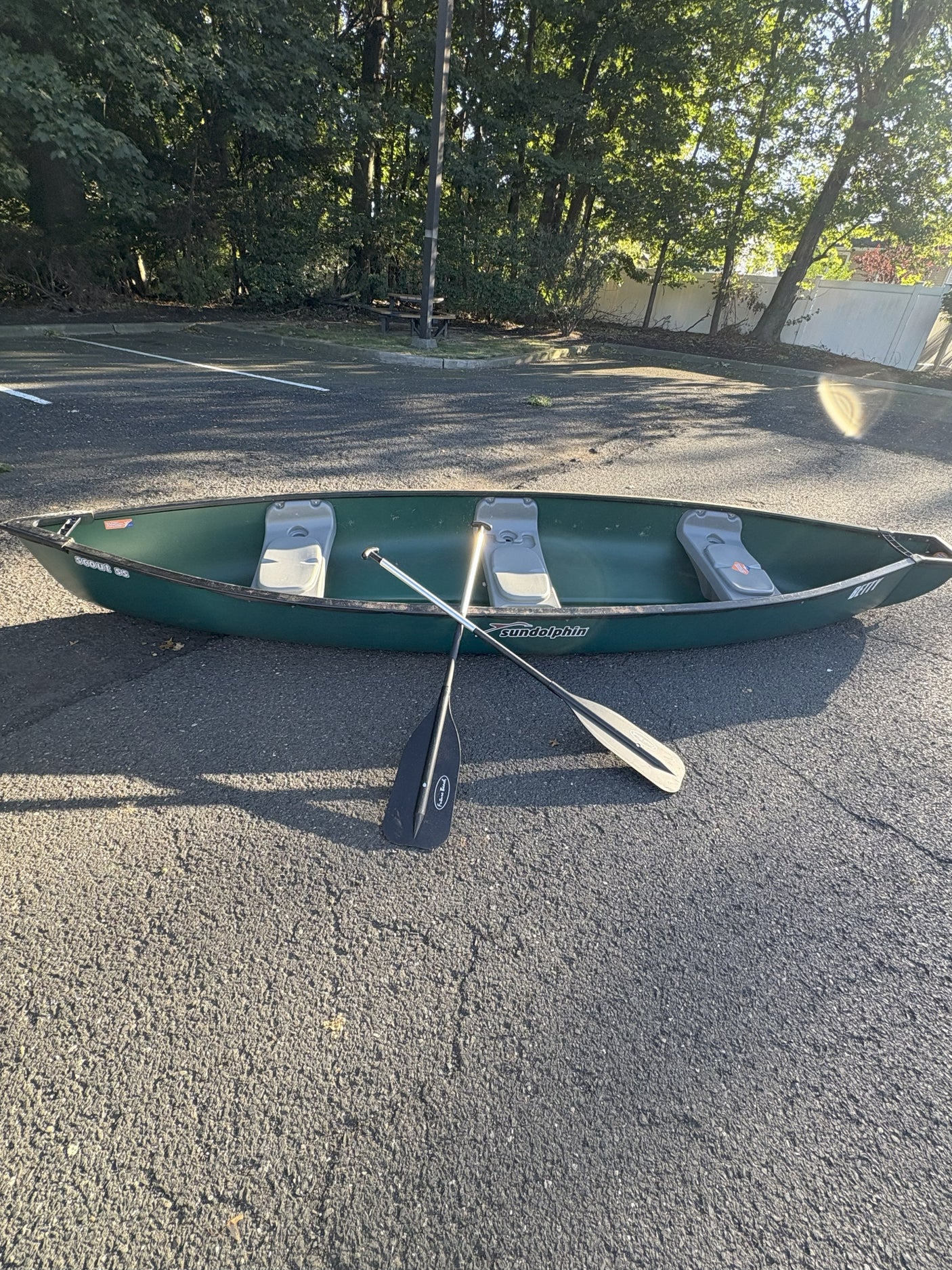Green Sun Dolphin canoe & paddles, parked on asphalt. Enhance your outdoor adventure with an RV rental!